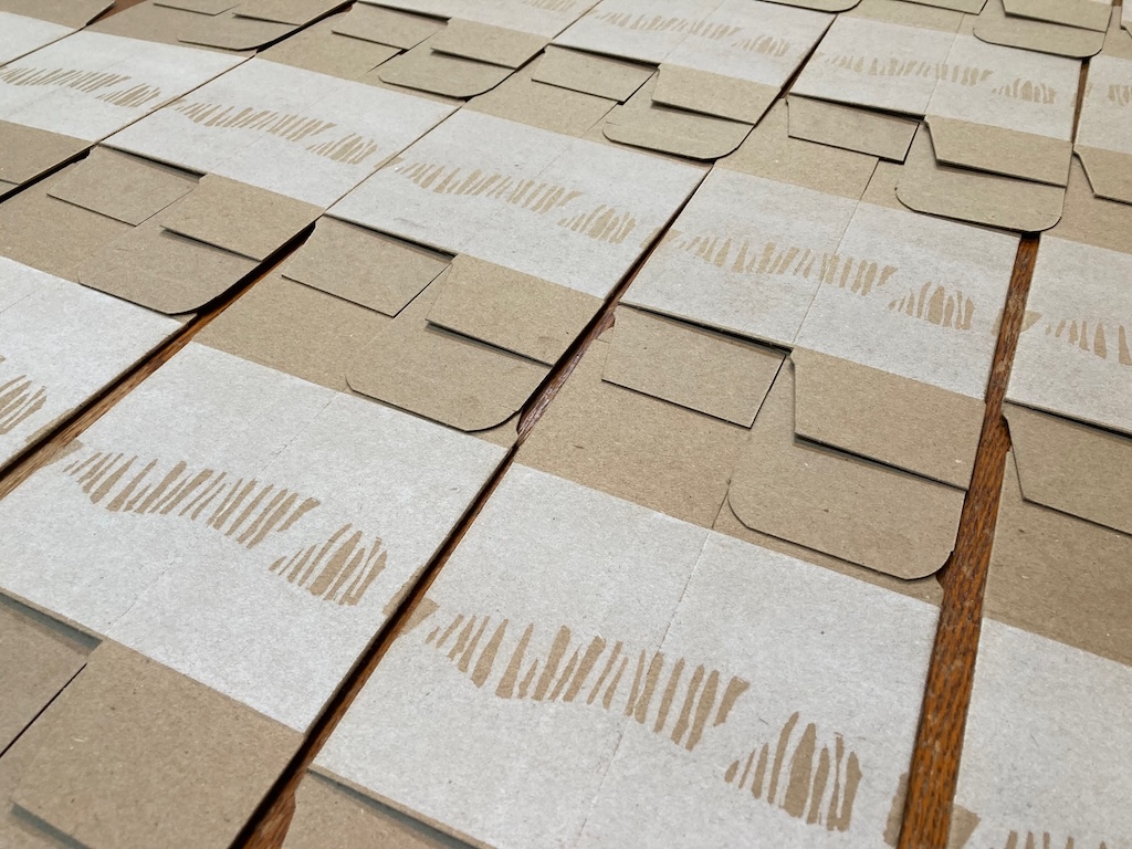 Brown cardboard boxes printed with white ink, set out to dry on a table,