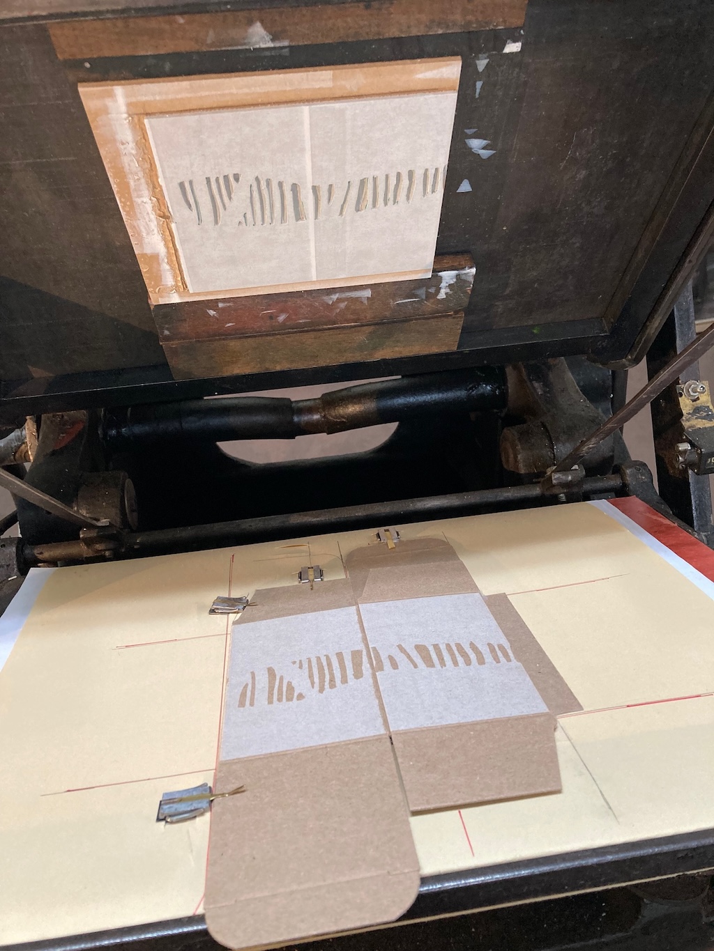 The lino block on the printing press, covered in white ink; below is the printed cardboard box with the white layer.