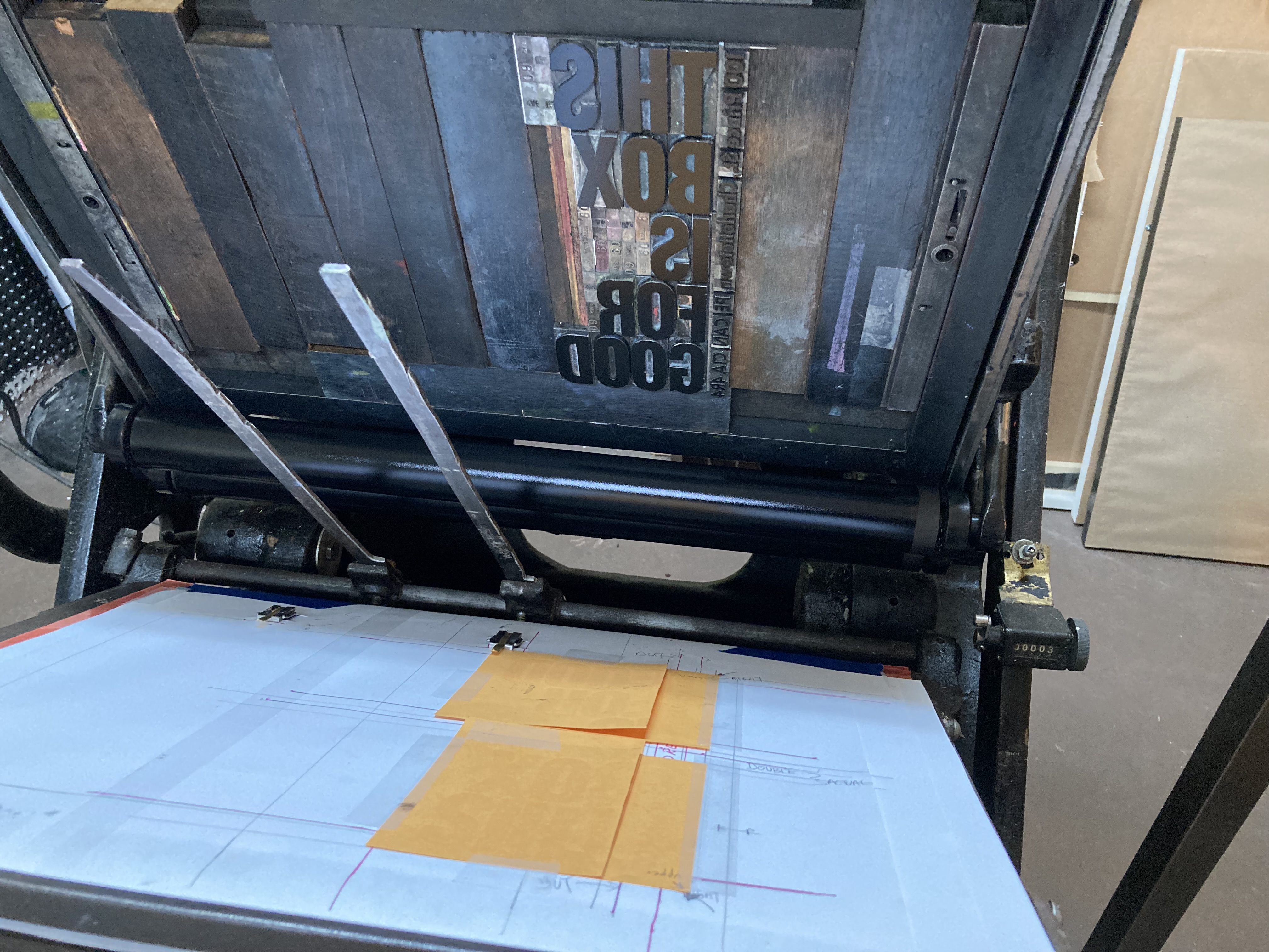 Yellow pieces of envelope paper set on the platen of a Golding Jobber No. 8 letterpress, with the type in the background, already inked and ready to print.