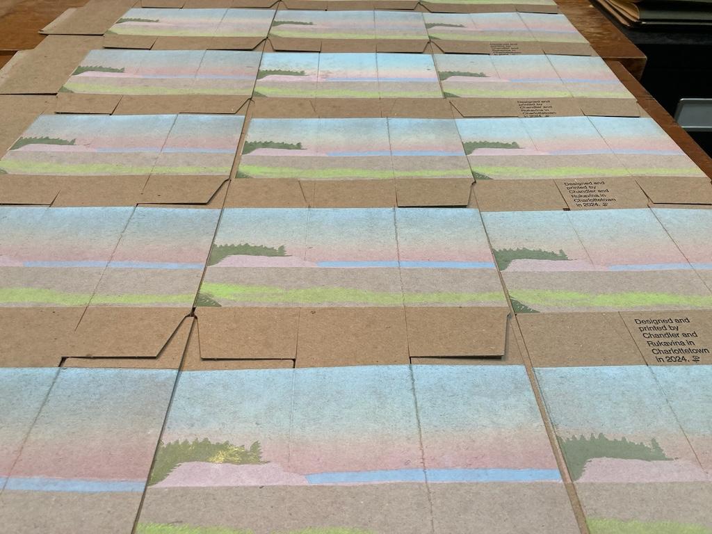 A pile of boxes with blue and greens printed, drying on a table.