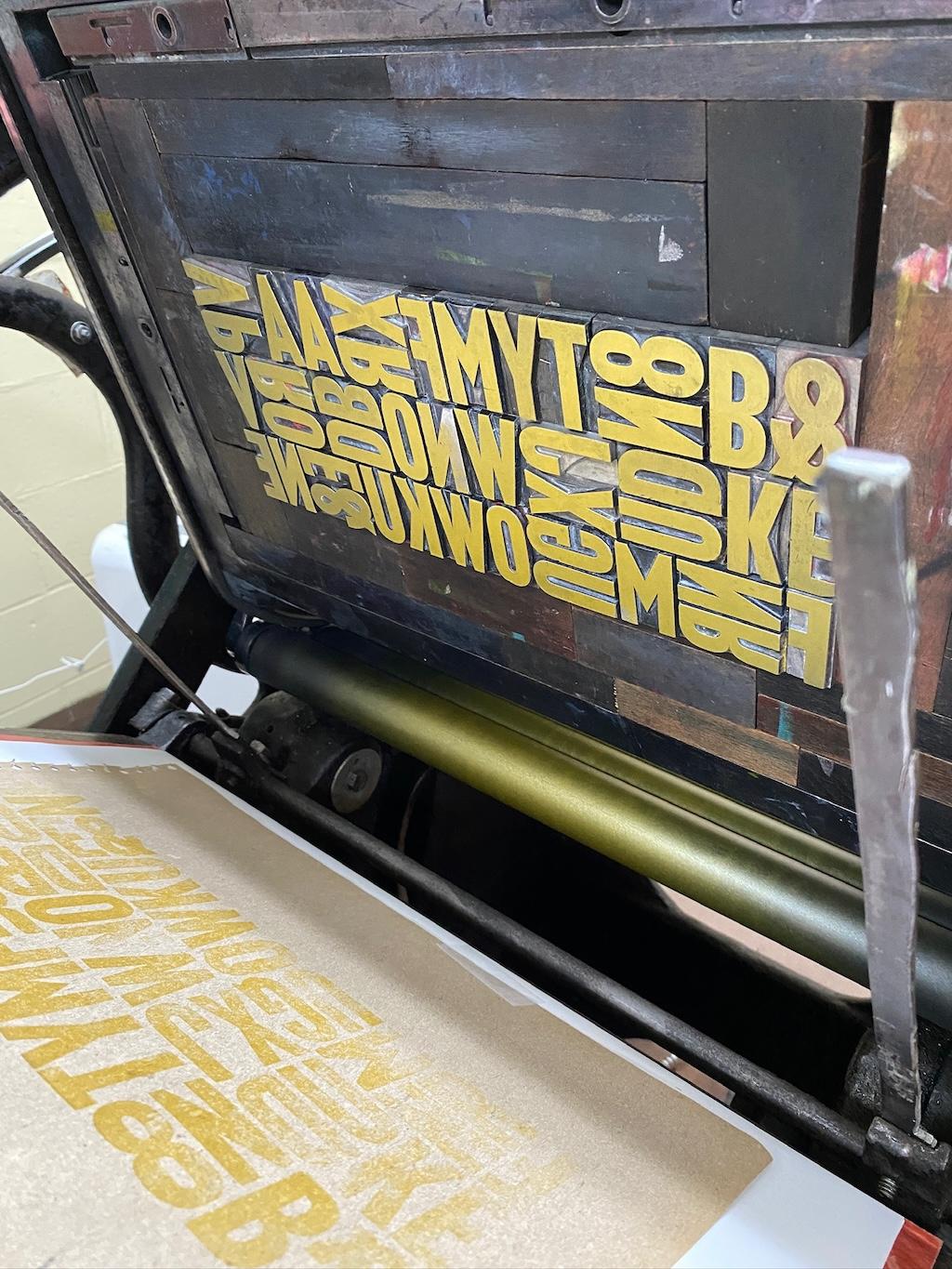 Metal type in the chase, covered with gold ink, with a box printed on the platen.