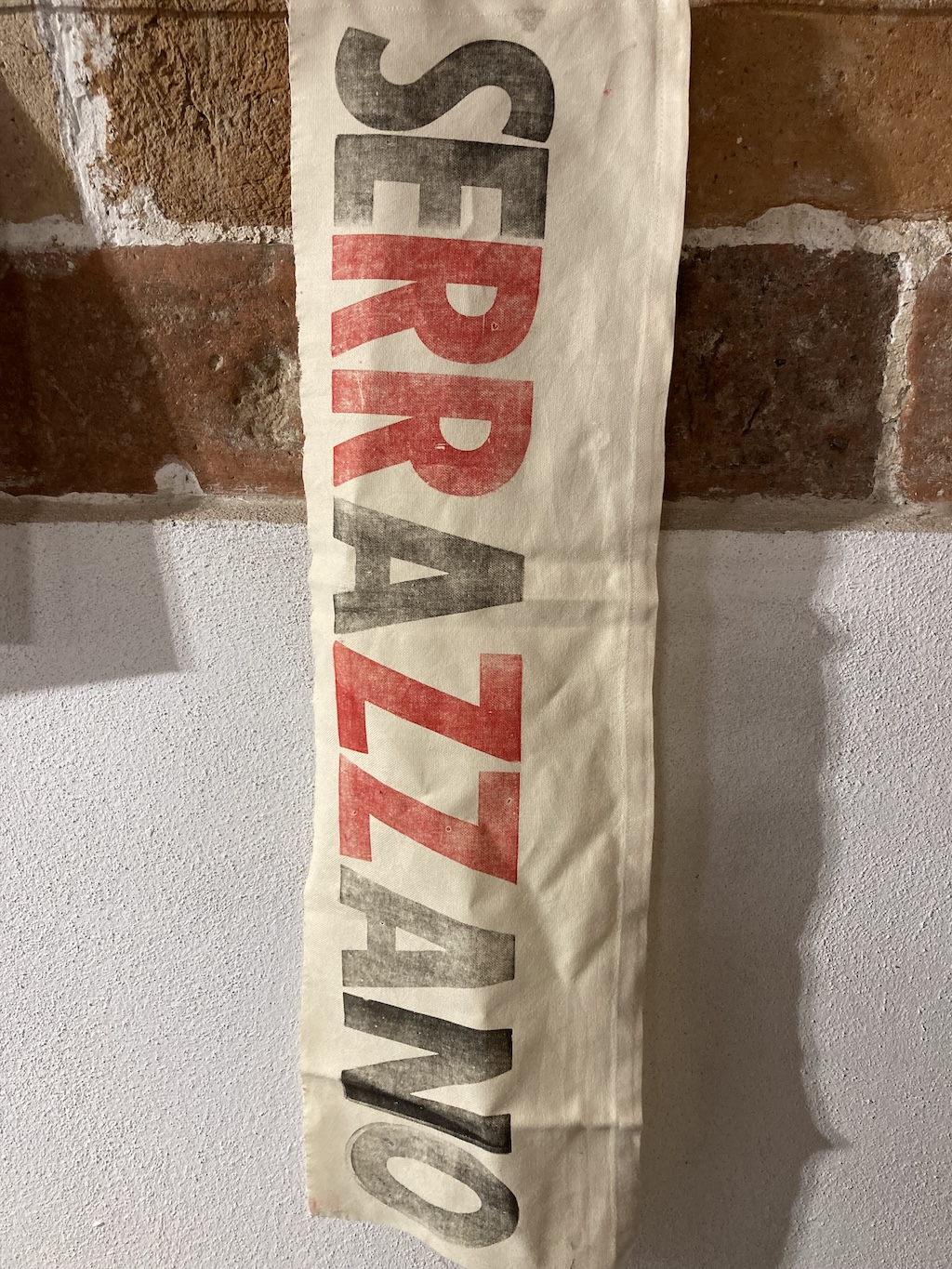 A Serrazzano banner printed in black and red, with large wood type, on beige linen.