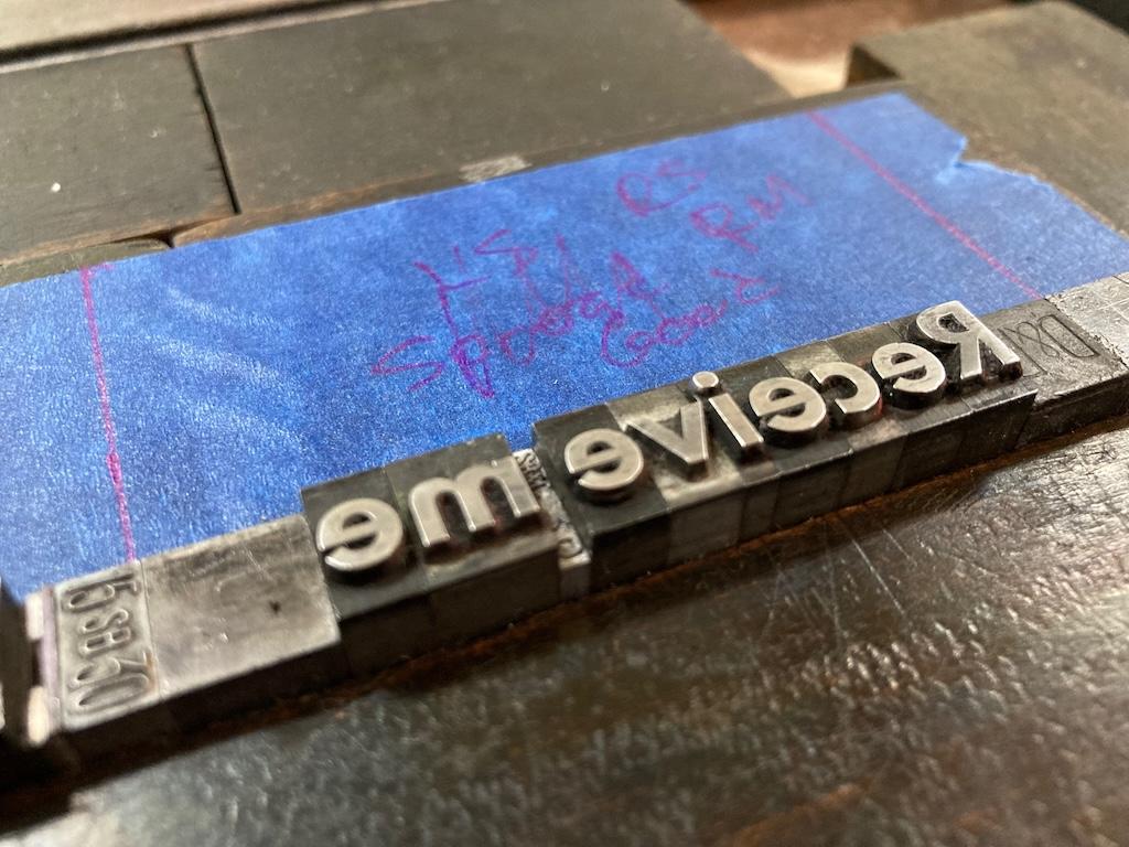 The words "Receive me" in metal type--reading right to left--set in the chase and ready to print.