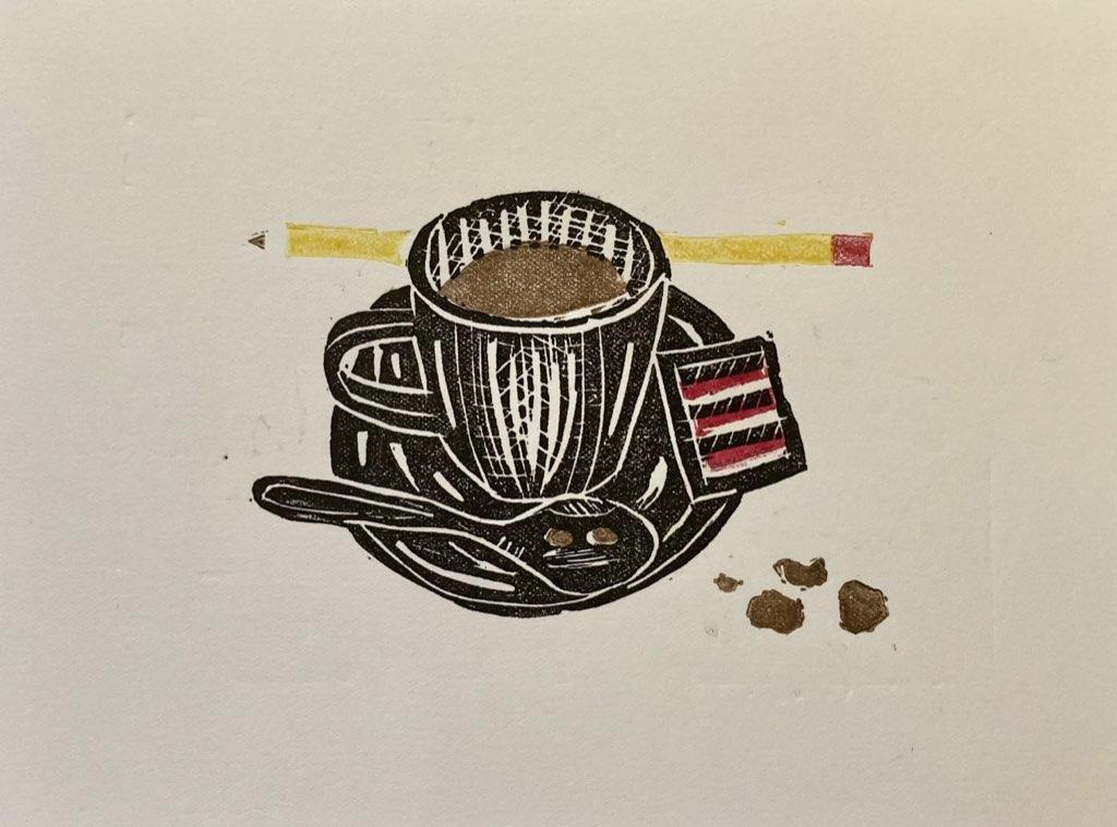 A lino print of a small cup of coffee sitting on a saucer, with a sugar packet on the saucer and a pencil in the background.