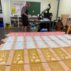 Three colours of the printed box, set to dry, with Peter at the press behind.