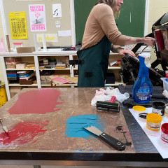 Ink rolled out in the foreground; Lori Joy Smith printing on the press behind.