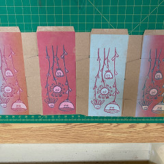 Four colours of the printed box, laid side by side, on a cutting mat.