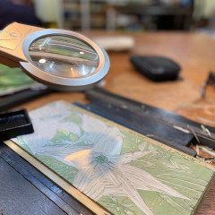 The lino block being carved, with magnifier overhead.