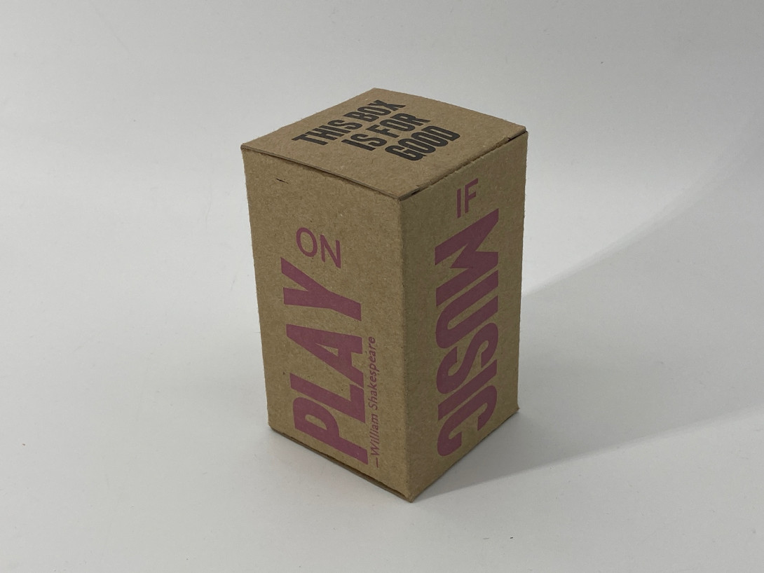 A brown cardboard box on a white background. On the left-hand side, in large pink letters, is the word PLAY; on the right hand side is the word MUSIC.