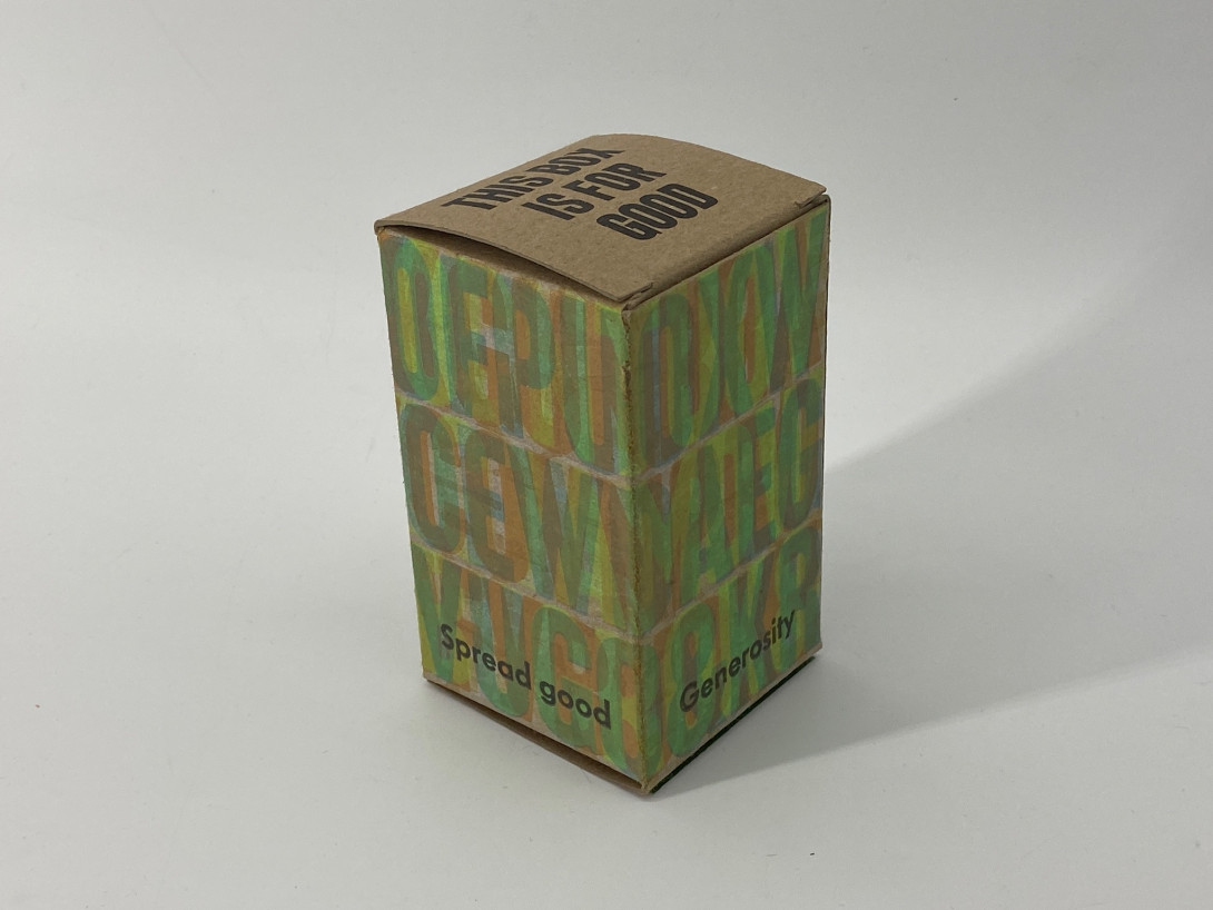 A brown cardboard box on a white background. Printed on the box, and a variety of overlapping colors, are large capital letters