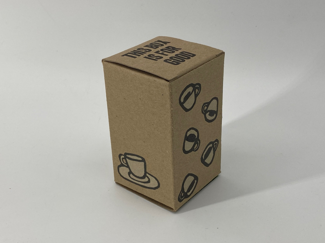 A brown cardboard box against a white background. On the top flap of the box are the words "this box is for good" in all caps. On the left side of the box is a printed image of a single espresso cup; on the right side there are images of falling coffee cups.