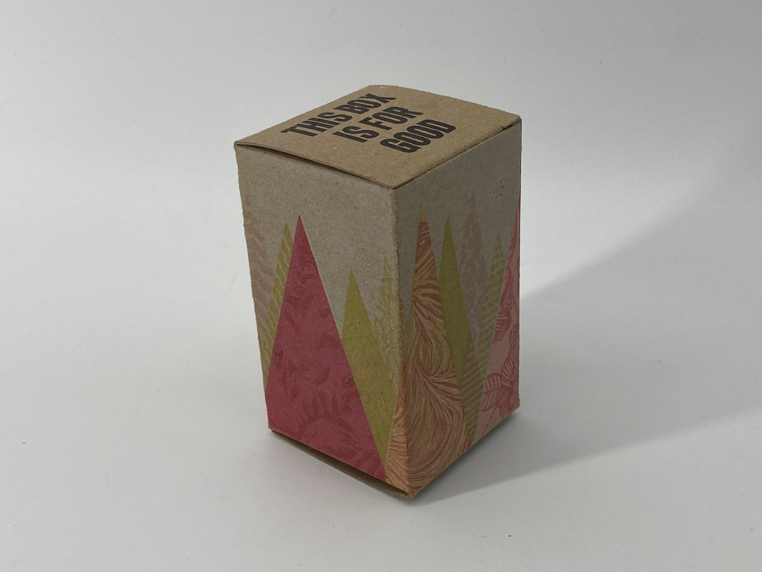 A brown cardboard box on a white background. Printed on the box, and shades of gold, red, pink, and white, are abstract Christmas trees