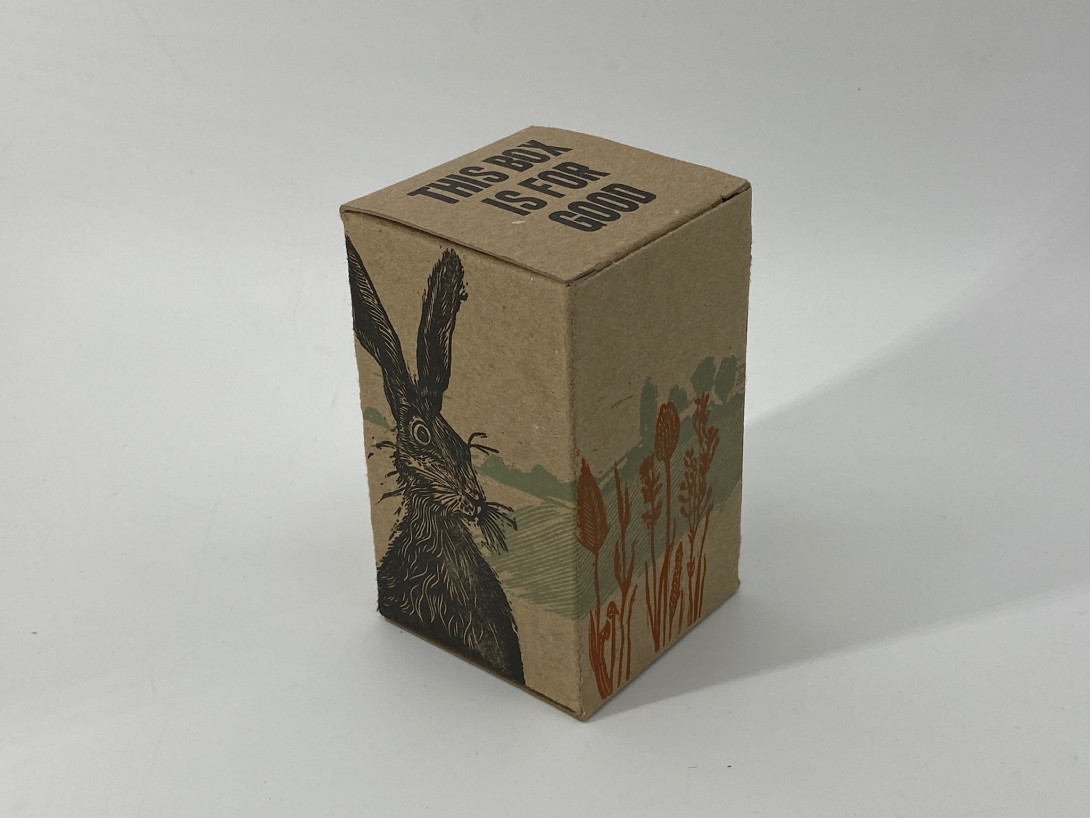 A brown cardboard box on a white background. Printed on the box, on the left, in black, is a hare; on the right, in blue and orange, is the scene of a field
