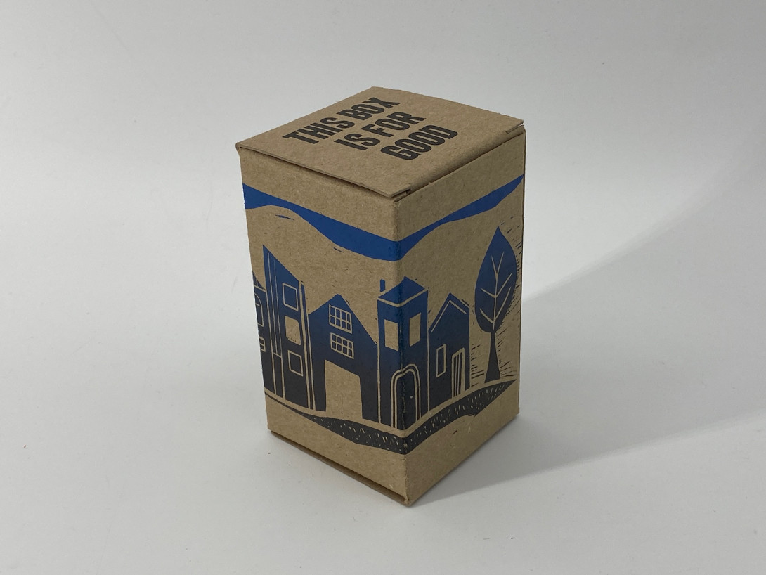 A brown cardboard box on a white background. Printed on the box, and shades of blue, is an abstract townscape